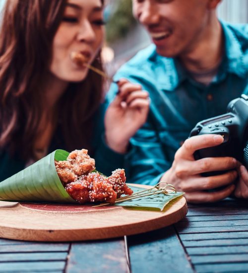 Happy young chinese couple sitting at cafe outside enjoying traditional asian food and watching pictures in photo camera.